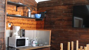 A compact kitchen with a microwave, coffee maker, and sink. There is a wooden table and a TV mounted on the wall. - Lofoten Camp Storfjord (Vestvågøy)