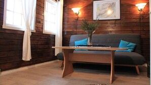 A cozy room with wooden walls, a sofa with blue cushions, a wooden coffee table, and two wall-mounted lamps. - Lofoten Camp Storfjord (Vestvågøy)