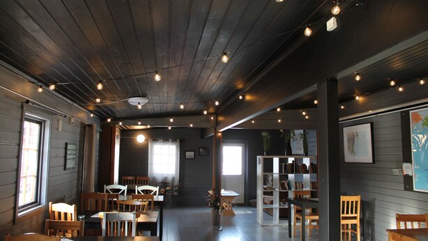 A cozy restaurant with wooden tables and chairs, a bookshelf, and string lights on the ceiling. - Lofoten Camp Storfjord (Vestvågøy)