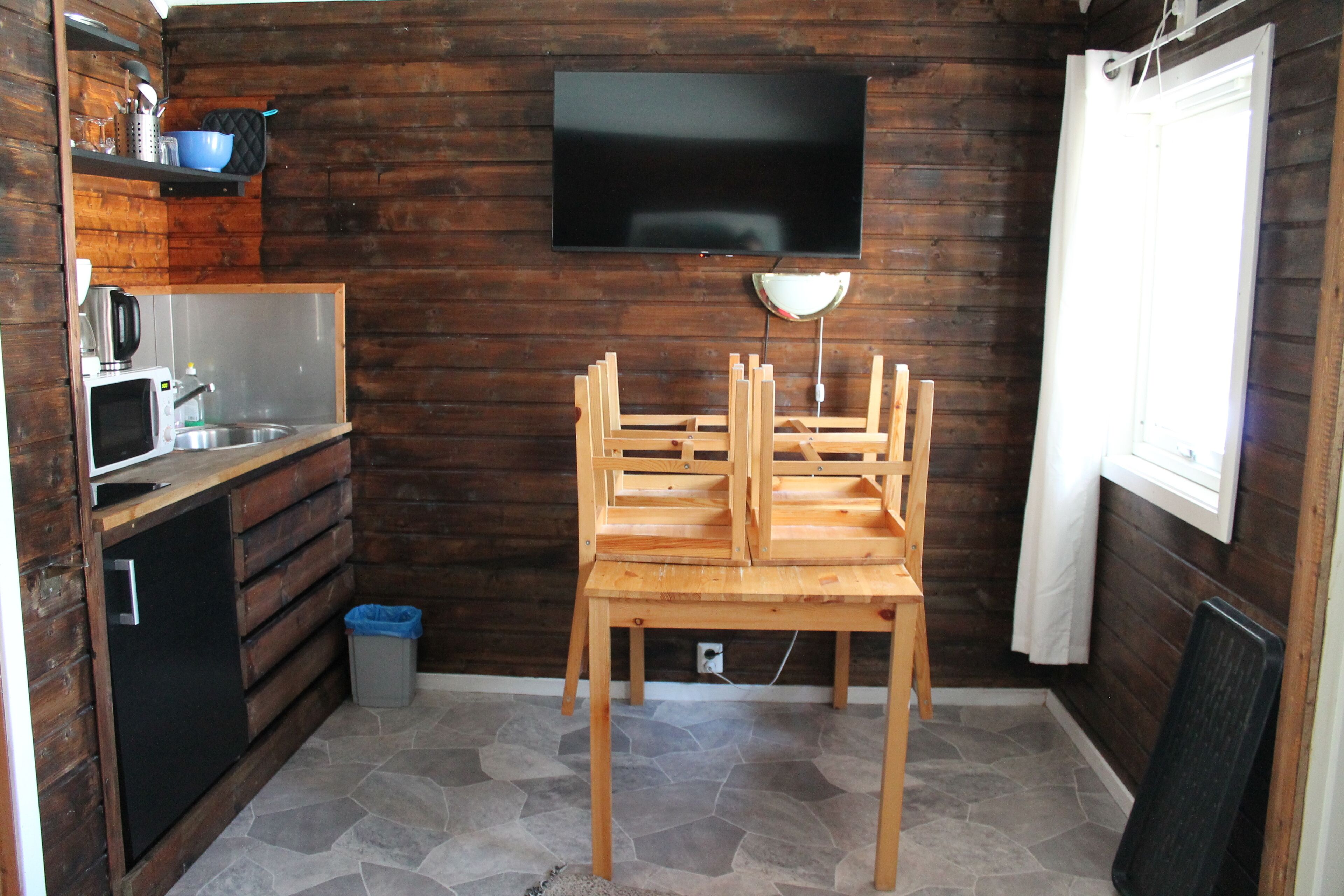 Cocina compacta con pared de madera, televisor de pantalla plana, un lavabo y zona de comedor con sillas.