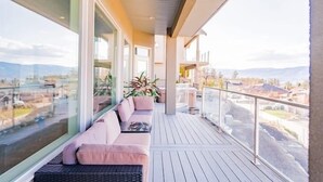A balcony with a sofa and potted plants, overlooking a residential area. - Legal Lakeview 2-bed 2-bath Entire Suite (Kelowna)