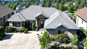 A residential house with a garage, a driveway, and a view of a lake and mountains. - Legal Lakeview 2-bed 2-bath Entire Suite (Kelowna)