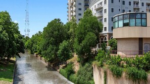 A river running alongside a modern building with balconies and a stone wall.