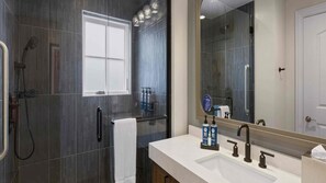 Une salle de bain moderne dotée d’une douche à parois de verre, d’un grand miroir et d’un meuble-lavabo avec un évier et un porte-serviettes.