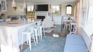 Une cuisine spacieuse dotée d’un îlot central, de tabourets de bar blancs, d’une cheminée et d ’un coin repas avec une table et des chaises.