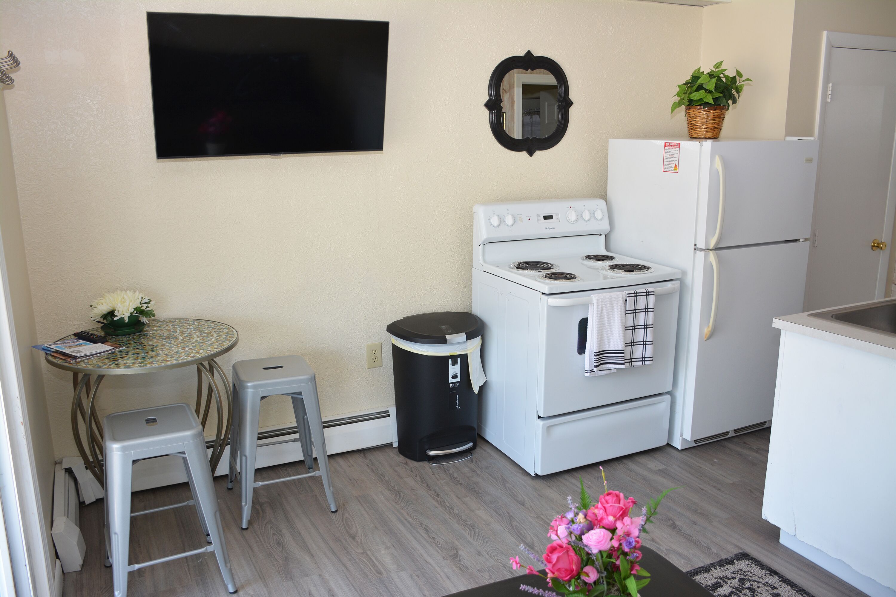 A compact kitchen with a stove, refrigerator, and a small dining table with two stools.