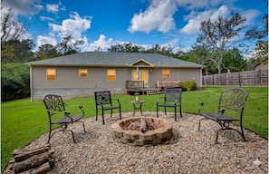 A house with a fire pit, four metal chairs, and a wooden deck.