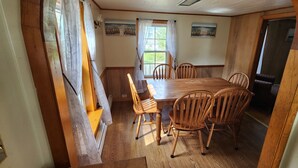 Une salle à manger avec une table et des chaises en bois, une fenêtre avec des rideaux et un tableau au mur.