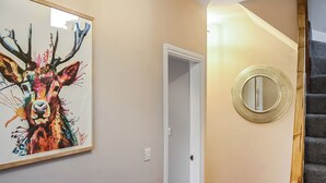 A hallway with a framed painting of a deer, a door, and a round mirror on the wall.