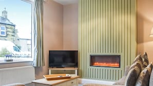 A cozy living room with a fireplace, a television on a stand, and a view of a building outside.
