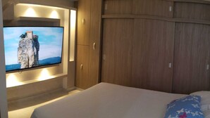 A bedroom with a bed, a TV mounted on the wall, wooden wardrobe, and a view of a rocky cliff. - Hermoso Apatamento CON Aire Neiva (Neiva)