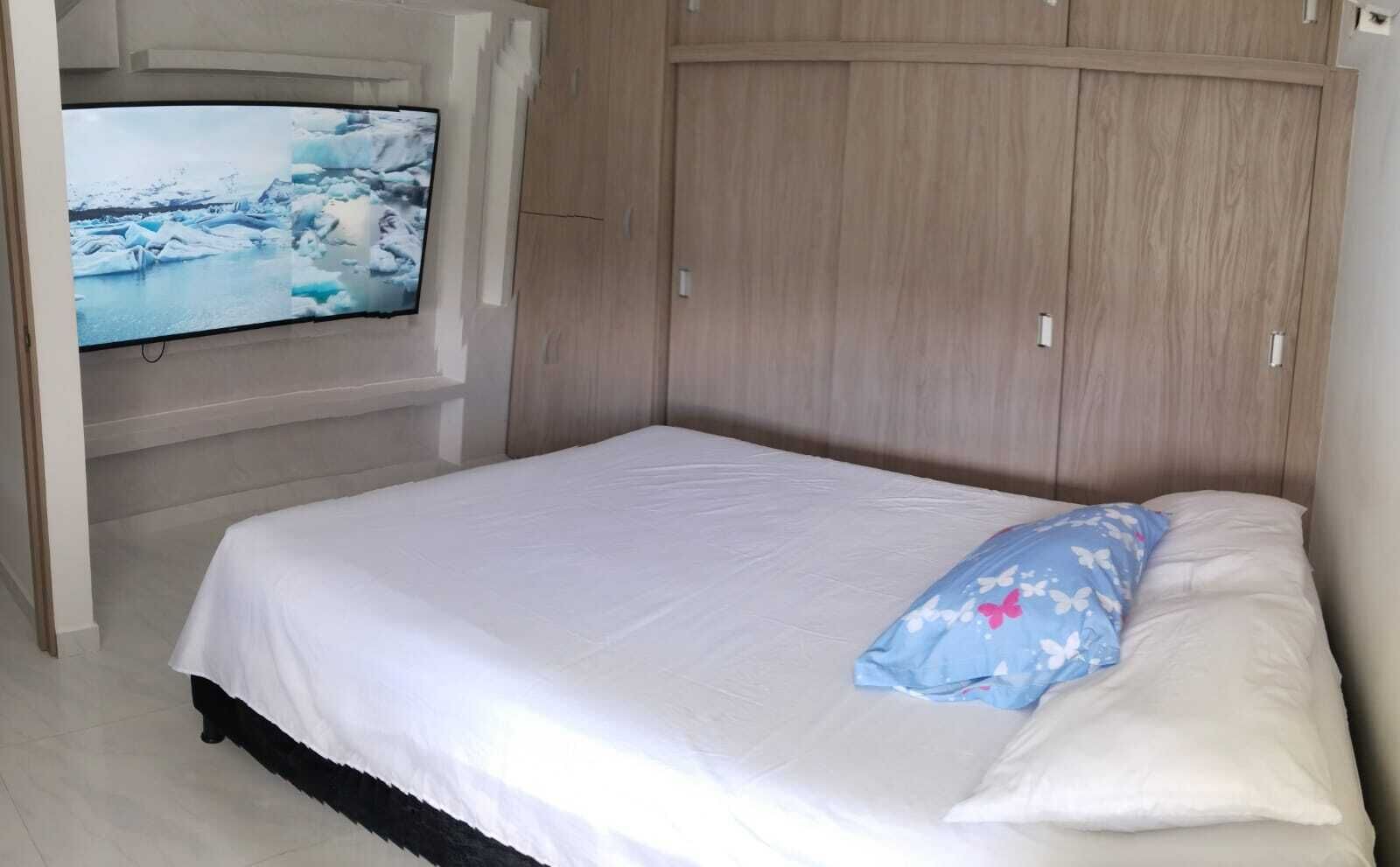 A bedroom with a bed, a TV mounted on the wall, and wooden cabinets.
