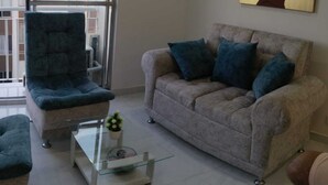 A living room with a sofa, armchair, and a glass coffee table with a plant. - Hermoso Apatamento CON Aire Neiva (Neiva)