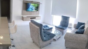 A modern living room with a flat-screen TV mounted on the wall, a dining table with chairs, and a sofa set. - Hermoso Apatamento CON Aire Neiva (Neiva)