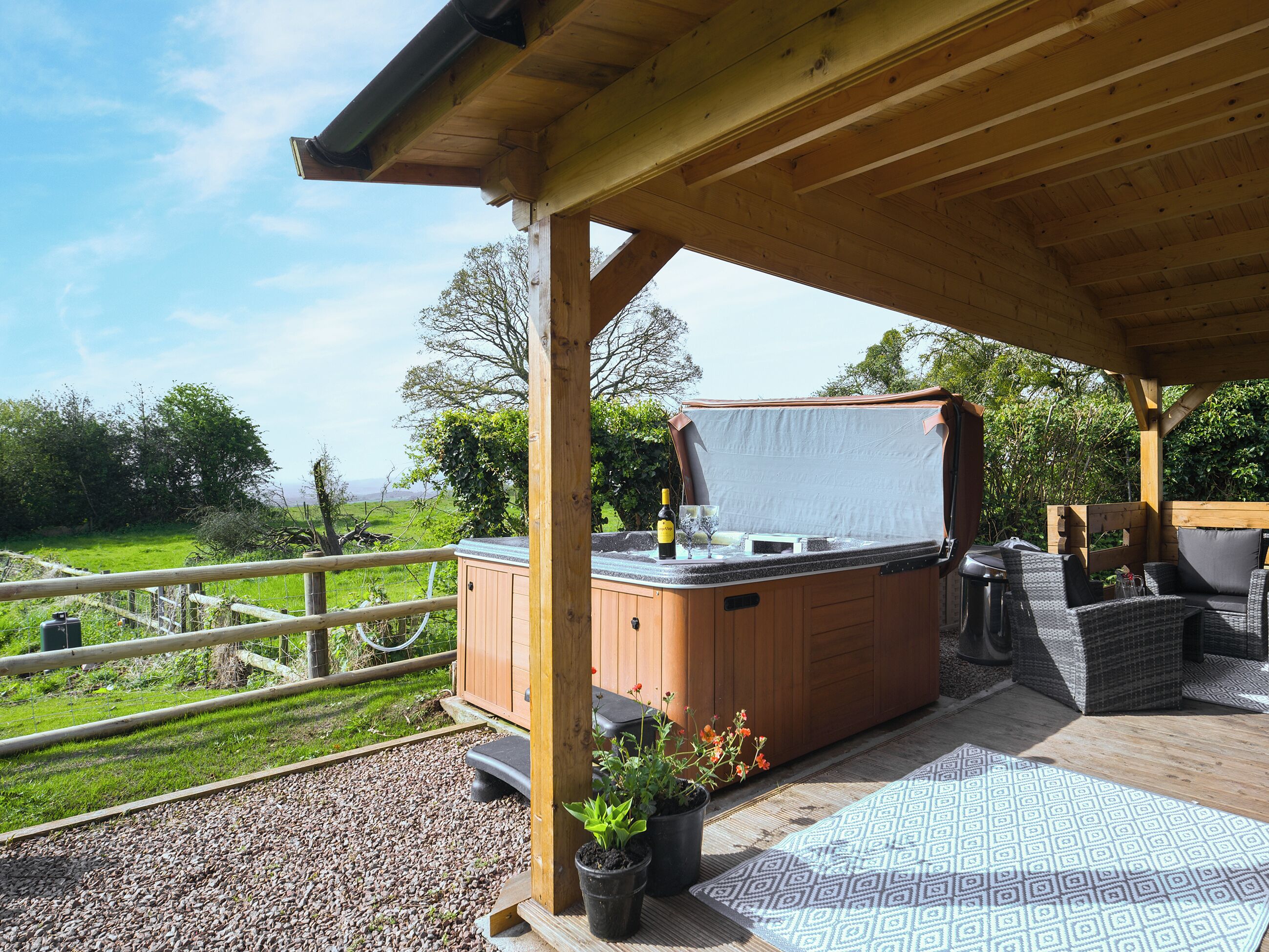 A wooden deck with a hot tub, outdoor seating, and a view of the countryside.