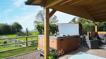 A wooden deck with a hot tub, outdoor seating, and a view of the countryside.