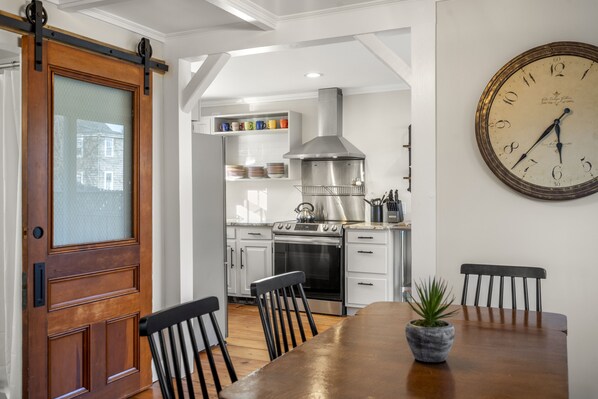 A kitchen with white cabinets, a stainless steel range hood, and a clock on the wall.