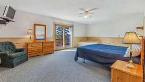 Ein Schlafzimmer mit Bett, Kommode, Stuhl, Fernseher und einem Balkon.