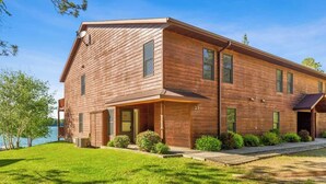 Ein zweistöckiges Holzhaus mit einer Veranda, einer Garage und einem kleinen Vorgarten mit Rasen und Sträuchern.