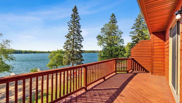 Eine Holzterrasse mit Geländer, die auf einen See mit umliegenden Bäumen blickt.