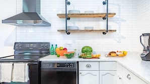 Une cuisine équipée d’une cuisinière, d’un lave-vaisselle et d’un plan de travail sur lequel sont disposés des fruits et des légumes.