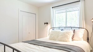 Une chambre à coucher avec un lit, une fenêtre avec des rideaux, une porte et une lampe fixée au mur.