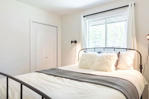 A bedroom with a bed, a window with curtains, a door, and a wall-mounted lamp. - Fun, Relaxing Cottage w Hot Tub, Sauna & Fast Wifi (Buckhorn)