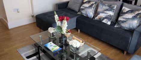 A living room with a dark sofa, a glass coffee table, and a white radiator in the background.