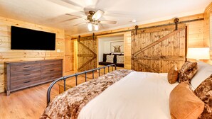 Een slaapkamer met een bed, houten wanden, een televisie en een plafondventilator.