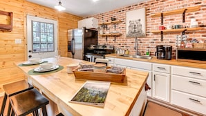 Een moderne keuken met houten keukenkastjes, een accentmuur van baksteen en een houten kookeiland met een deurmat en een tijdschrift.