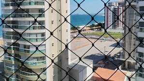 A high-rise building with a curved facade, a parking area, and a view of the sea. - Vista da Orla de Itapoã - 1002 (Itapuã Vila Velha)