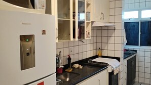A kitchen with white cabinets, a refrigerator, and a window. - Vista da Orla de Itapoã - 1002 (Itapuã Vila Velha)