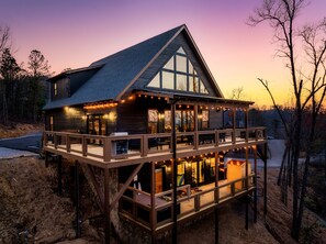 A two-story wooden cabin with a balcony, large windows, and string lights. - Luxe cabin. Pool, sauna, hot tub, pool table, pets (Sevierville)