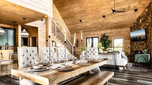 Un'ampia sala da pranzo con un tavolo di legno apparecchiato per quattro persone, una scala che conduce a un livello superiore e un muro in pietra con un televisore.