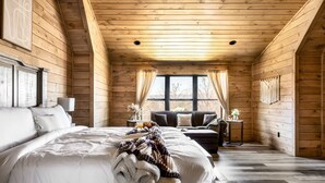 Camera da letto in una baita di legno, con un letto grande, un divano e un tavolino con una lampada.