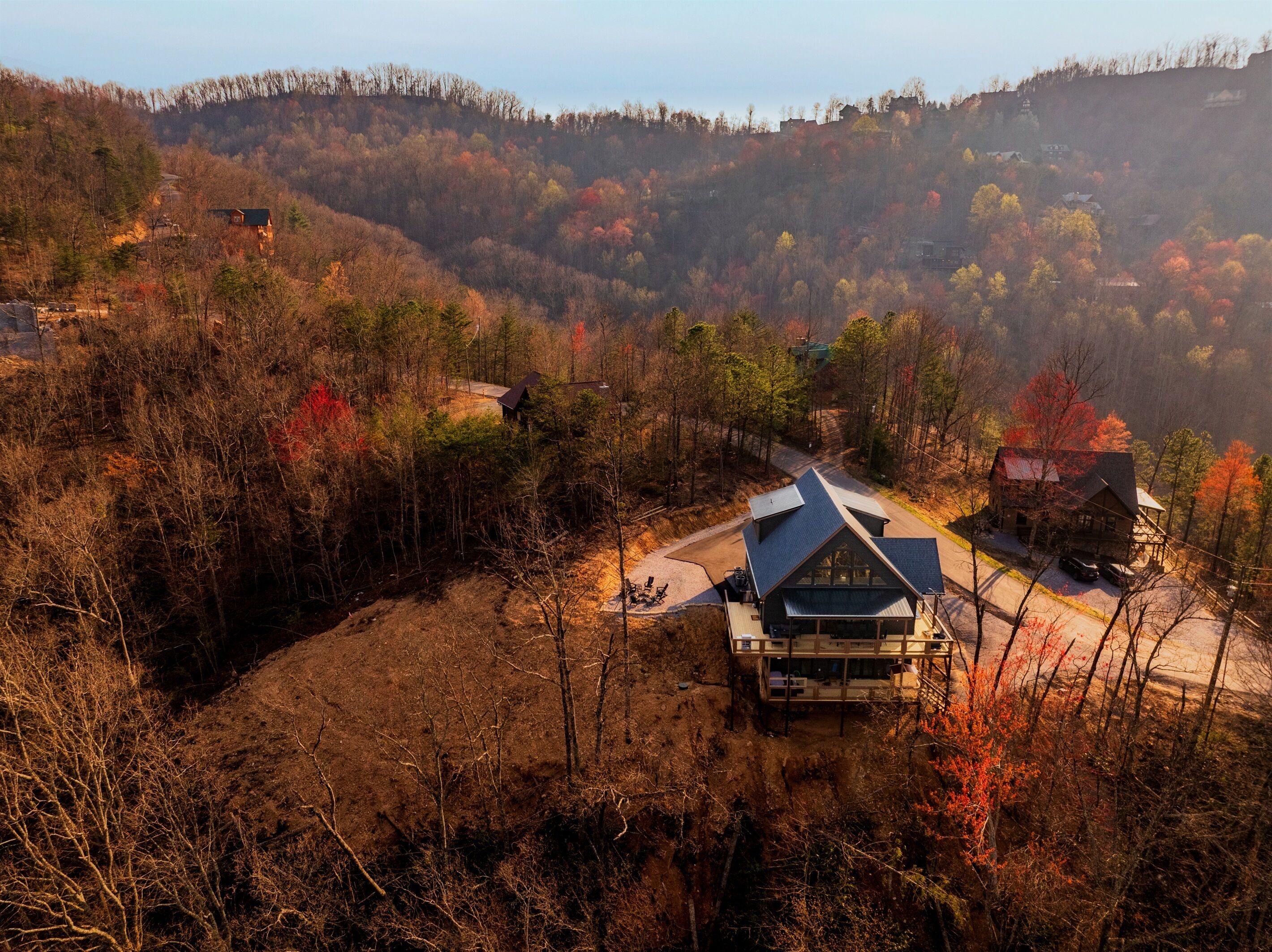 Une cabane au toit en pente, entourée du feuillage automnal et de collines.