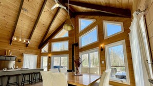A spacious wooden cabin with a large dining table, multiple windows, and a kitchen area. - Boutique chalet—woodland retreat, fireplace, chef kitchen, soaking tub—near PTDN (Val-Morin)