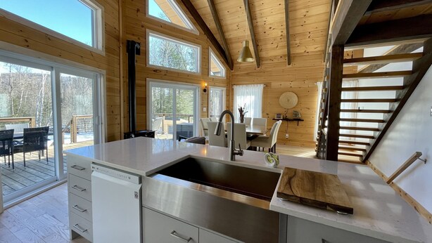 A modern kitchen with a large island, stainless steel appliances, and a view of the outdoors through large windows. - Boutique chalet—woodland retreat, fireplace, chef kitchen, soaking tub—near PTDN (Val-Morin)