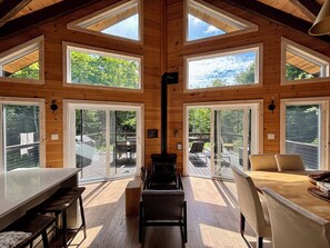 A wooden cabin with a dining area, large windows, and a deck. - Handcrafted Chalet with Fireplace & Chef's Kitchen (Val-Morin)