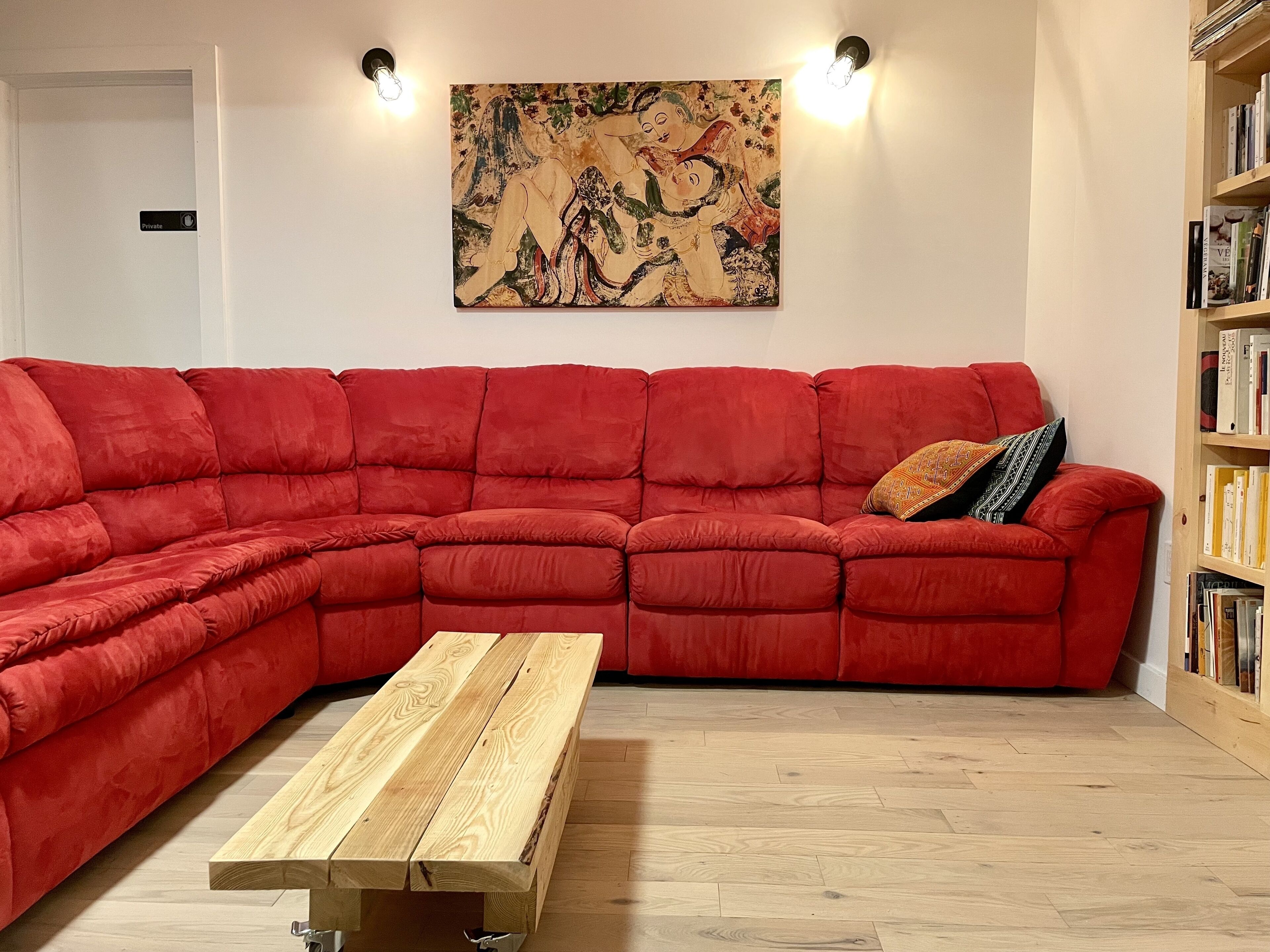 Een rode modulaire bank, een houten salontafel en een boekenkast vol boeken.