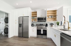 A modern kitchen with white cabinetry, stainless steel appliances, and a herringbone tile backsplash.