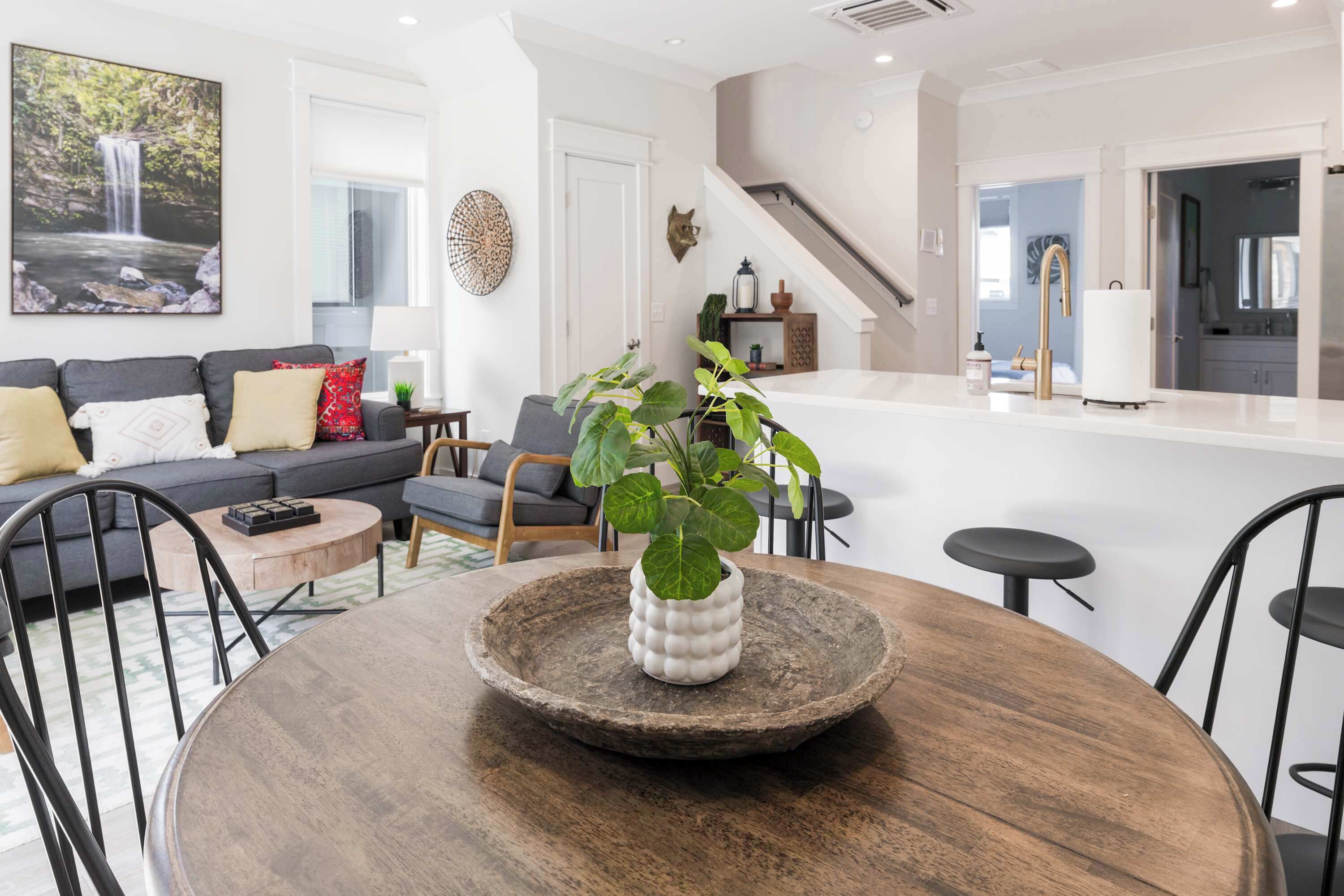 A modern living room with a dining area, a kitchen with a white countertop, and a staircase leading to another level.