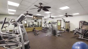 Een sportschool met diverse fitnessapparaten, plafondventilatoren en een grote spiegel.