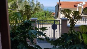 A residential area with a gated entrance, a house with a red-tiled roof, and a view of the sea.
