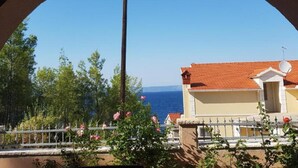 A balcony with a view of the sea, a building with a red-tiled roof, and a satellite dish.