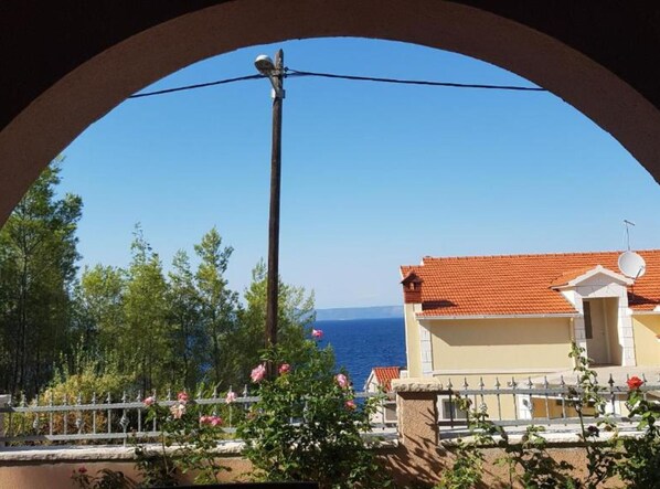 A balcony with a view of the sea, a building with a red-tiled roof, and a satellite dish.