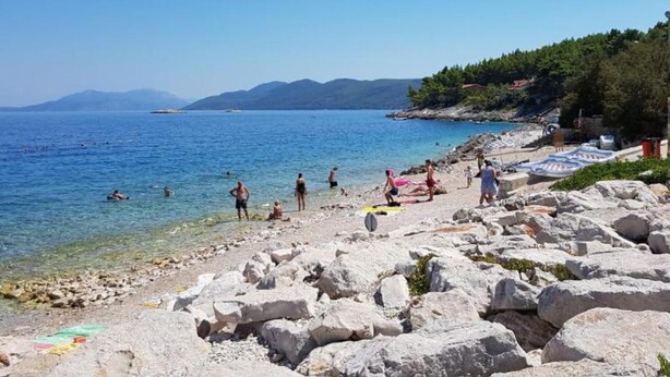 A rocky beach with clear blue water and a few people.