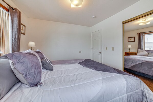 A hotel room with two beds, a large mirror, a door, and a window with blinds.
