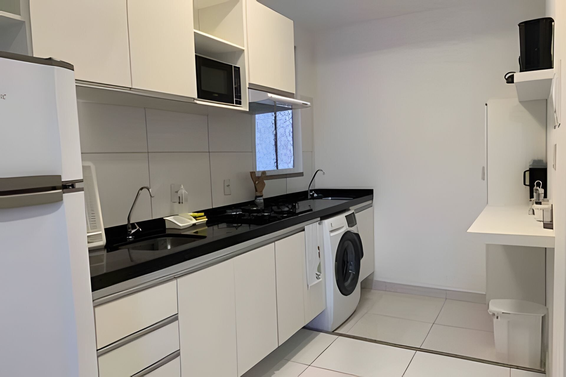 A modern kitchen with white cabinets, a black countertop, a built-in microwave, a washing machine, and a window with a view.