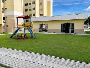 Um parquinho com uma estrutura de escalada e um prédio com entrada de vidro.
